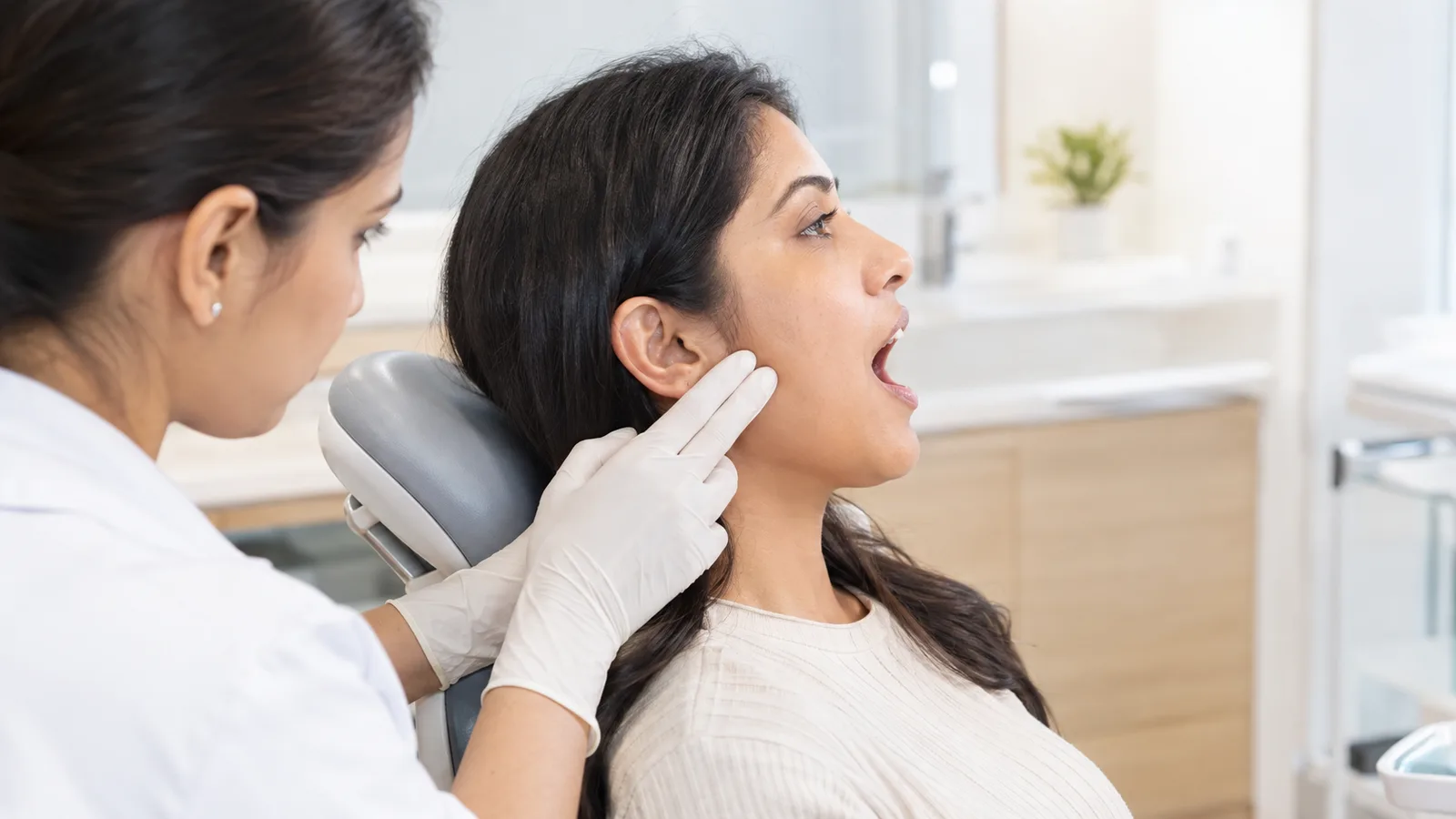 Dentist gently examining a patient's jaw joint in front of the ear in a dental clinic